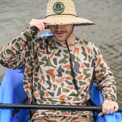 A man in canoe wearing a Gator Wader's Old School Camo Performance Shirt and Straw Hat