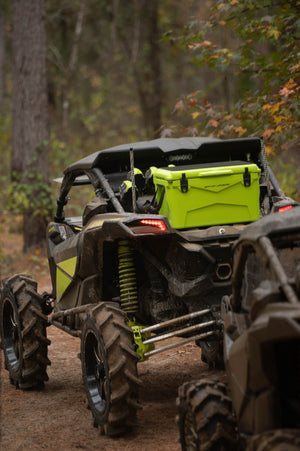 Image of a side-by-side riding trails with a Gator Wader's 45qt  Bounty Cooler in the color lime sitting in the back 