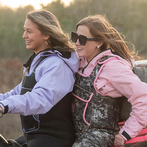 two women riding on the back of an ATV in purple and pink bogs and retro waders