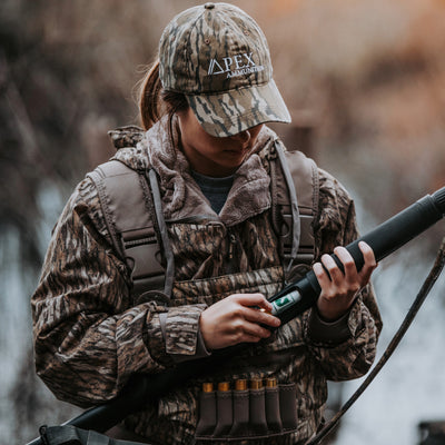 Woman holding a shotgun while hunting wearing bottomland camo waders