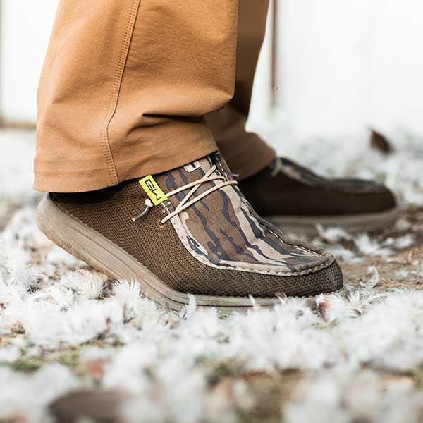A guy standing in goose feathers wearing a pair of Camp Shoes in Mossy Oak Bottomland.