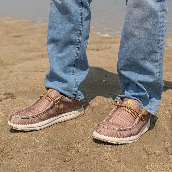 A guy standing in the sand on the beach with a pair of Camp Shoes on.
