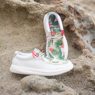 A pair of Camp Shoes sitting on the beach. The shoes are a tropical pattern.