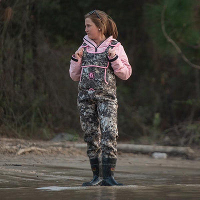 Woman walking by lake looking away while wearing Gator Waders Retro Waders in Seven camo with pink trim.