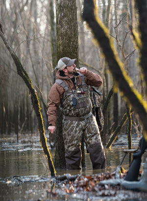 A guy standing in the timber wearing Gator Waders Shield Waders in Mossy Oak Original Bottomland.                                                                                                                                                                                                                                                                                        
